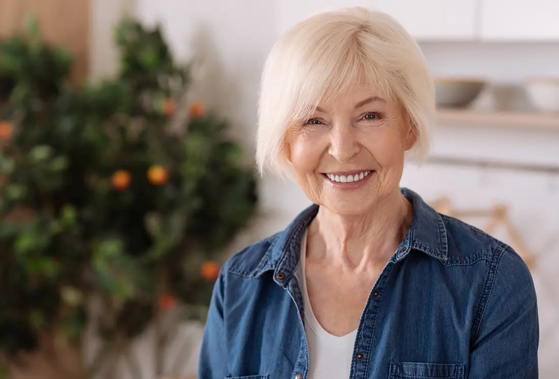 Joyful nice elderly woman smiling and standing in the kitchen