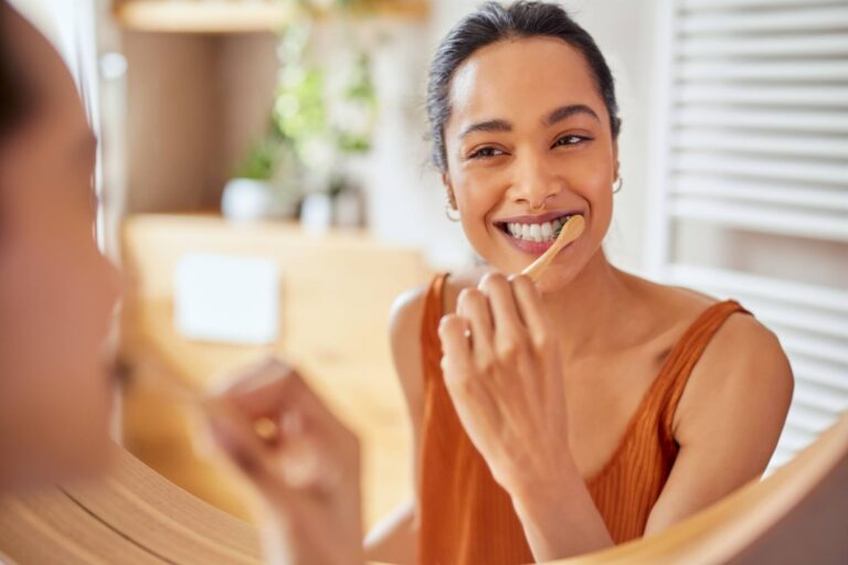 Smiling young woman brushing teeth in bathroom